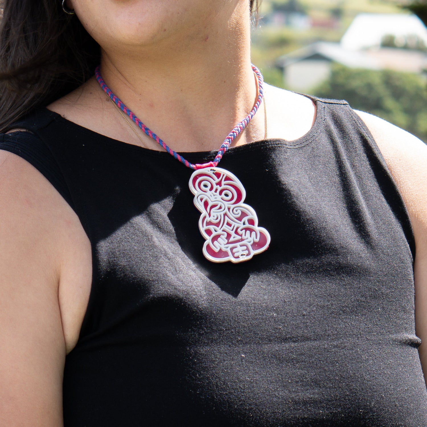Person wearing a black sleeveless top with a colorful necklace featuring a red and white pendant.