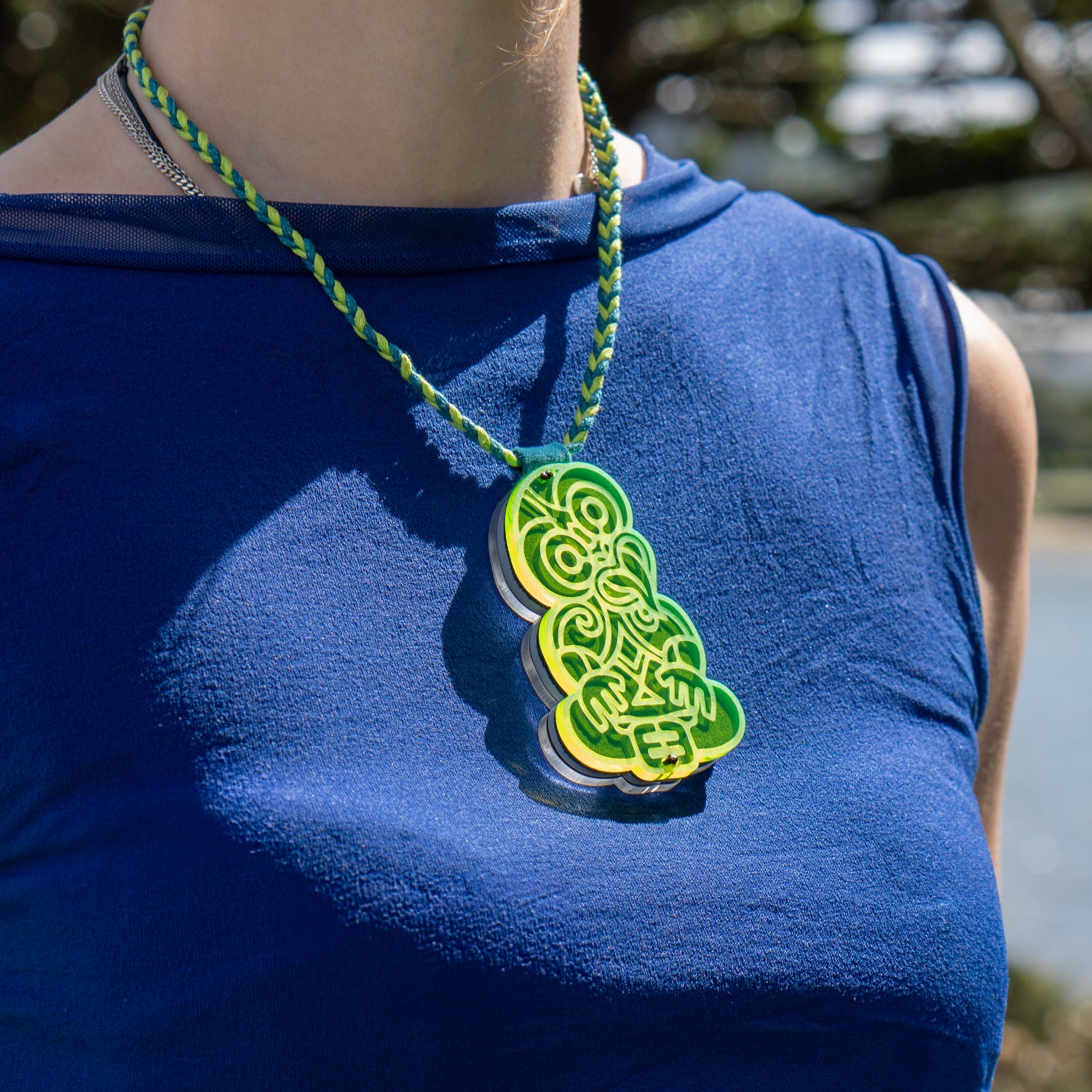 Person wearing a blue sleeveless shirt with a green pendant necklace.