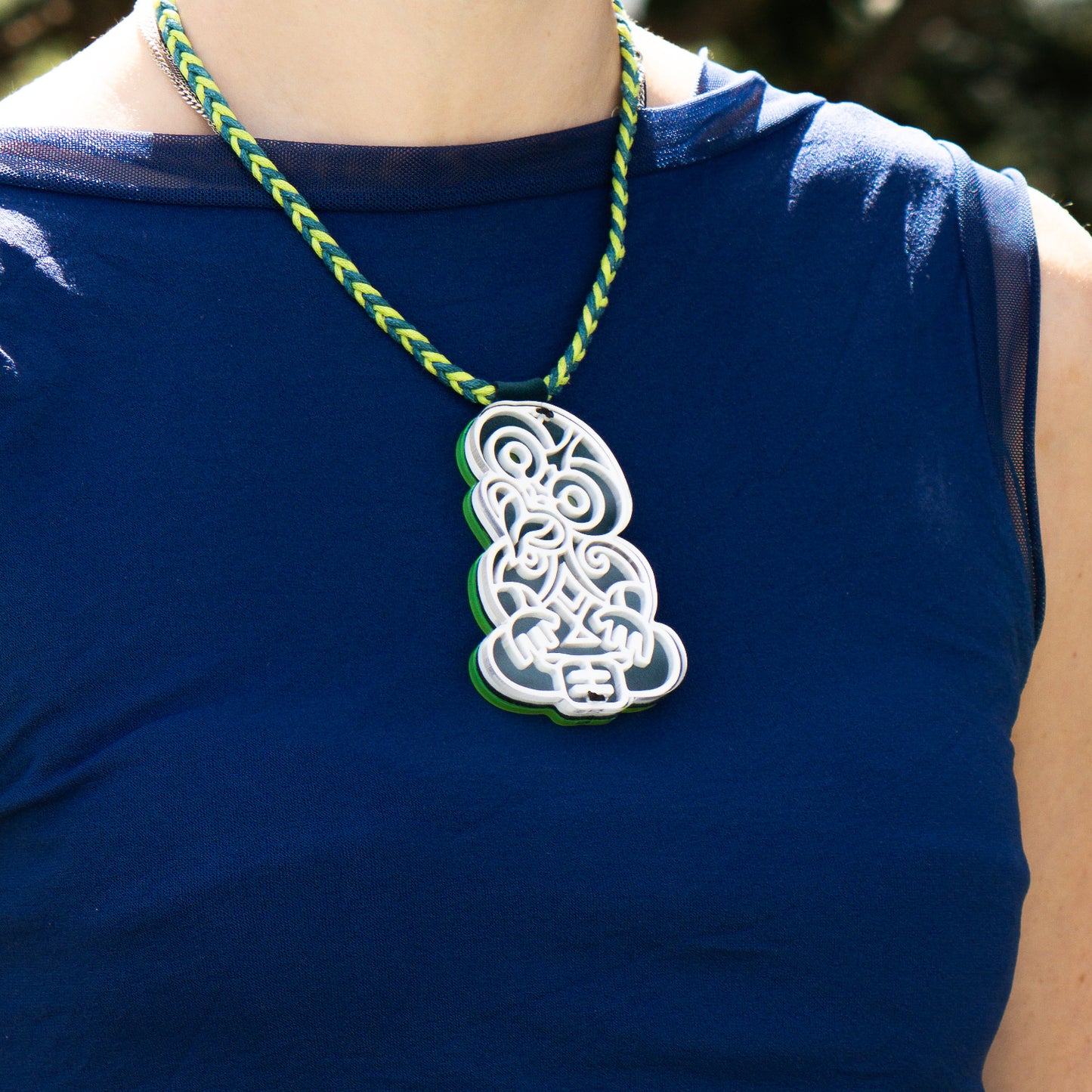 Person wearing a blue shirt with a green and blue braided necklace and a decorative pendant.