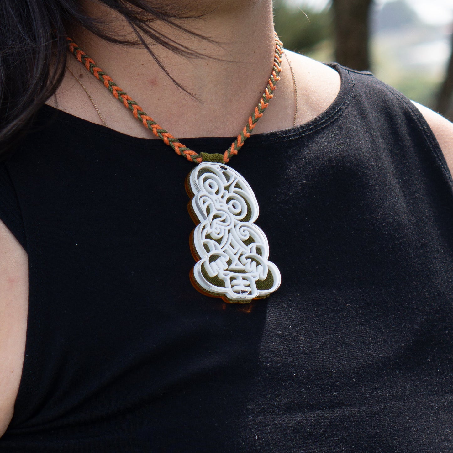 Person wearing a black top with a green pendant necklace
